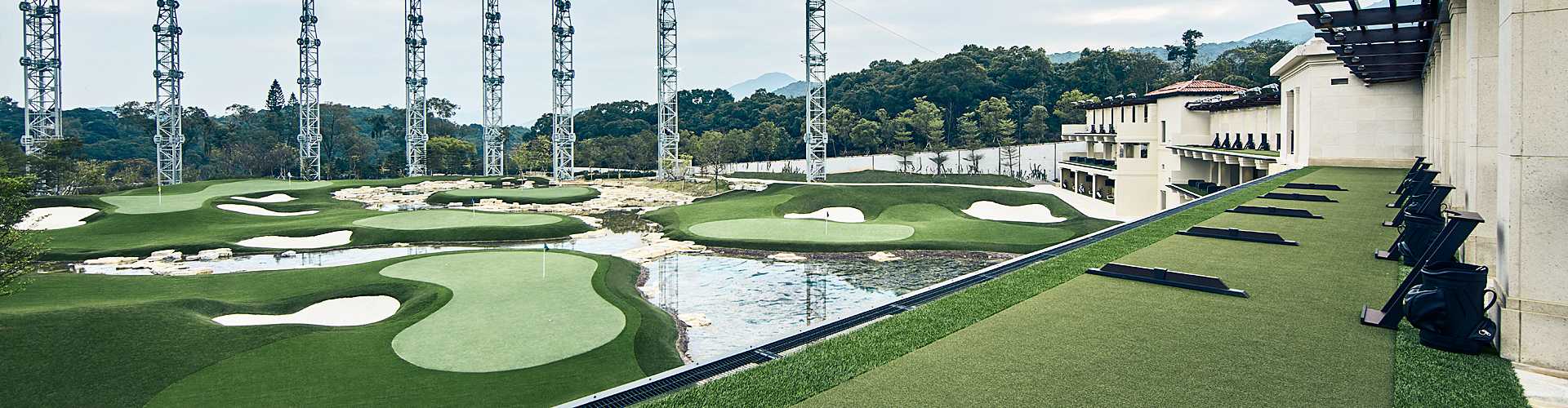 Large-scale artificial turf putting course with sand bunkers, water hazards, and driving range at a luxury resort golf facility