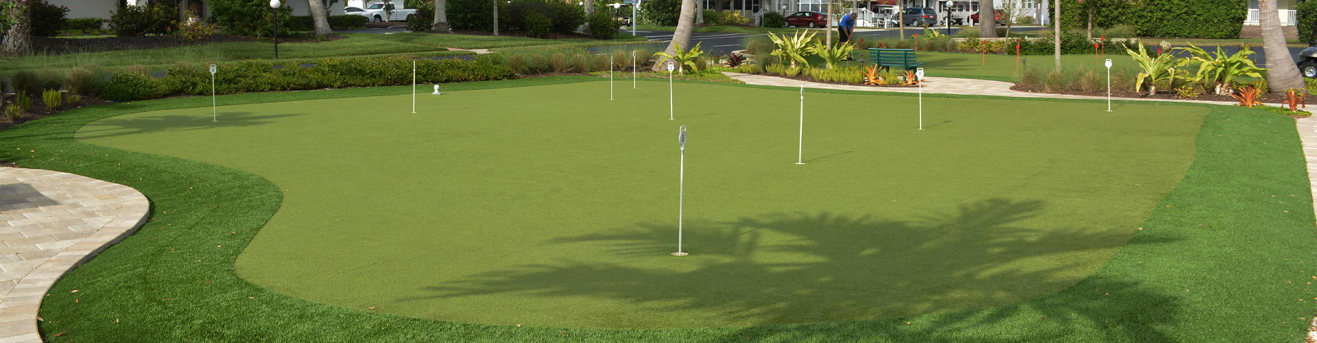 Multi-hole artificial turf putting green at a Florida community or golf club with paver border and tropical landscaping